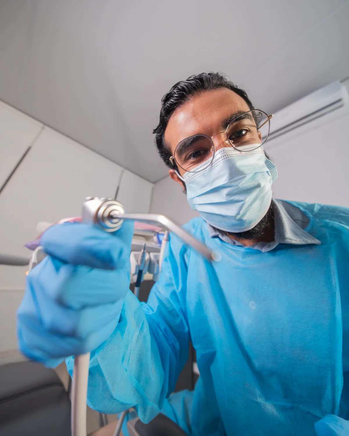 The dentist in mask and gloves holding the drill up to the lens, FLOOSS campaign still