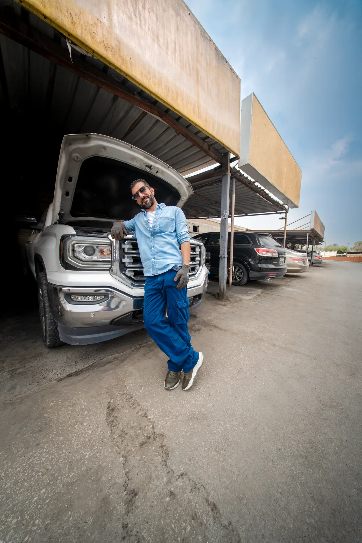 The mechanic leaning on the open bonnet of a white pickup in a Bahrain garage, FLOOSS Later? Why not campaign still
